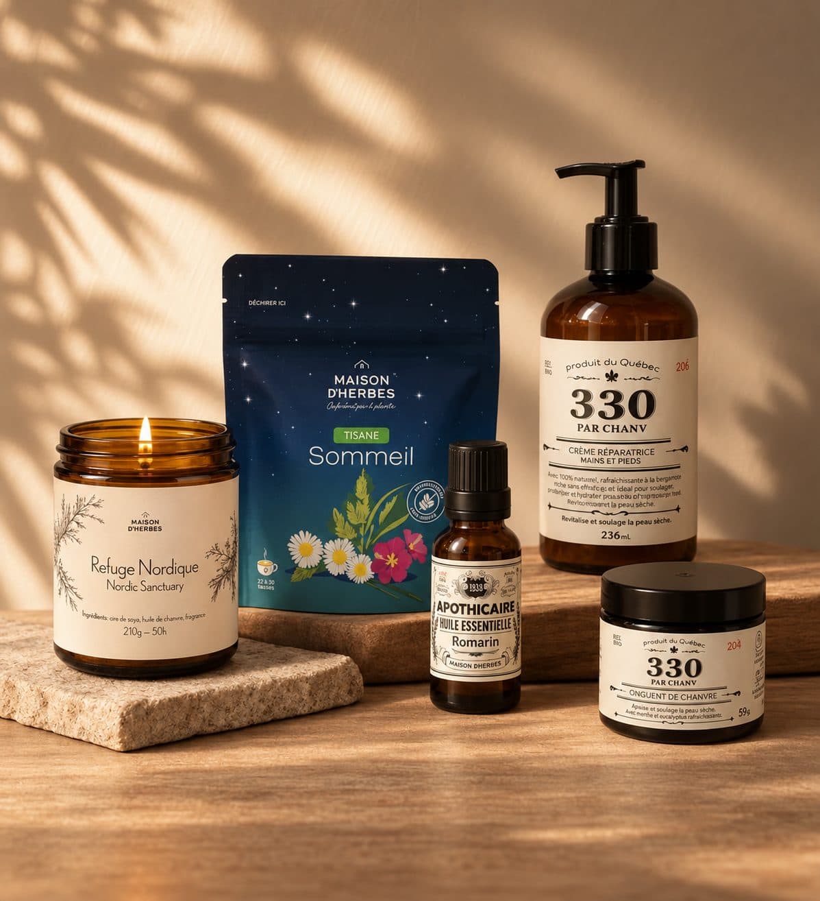 Cinq produits en ancien emballage sur une table de bois : bougie allumée, sachet de tisane Sommeil, crème mains et pieds, huile essentielle de romarin et onguent de chanvre
