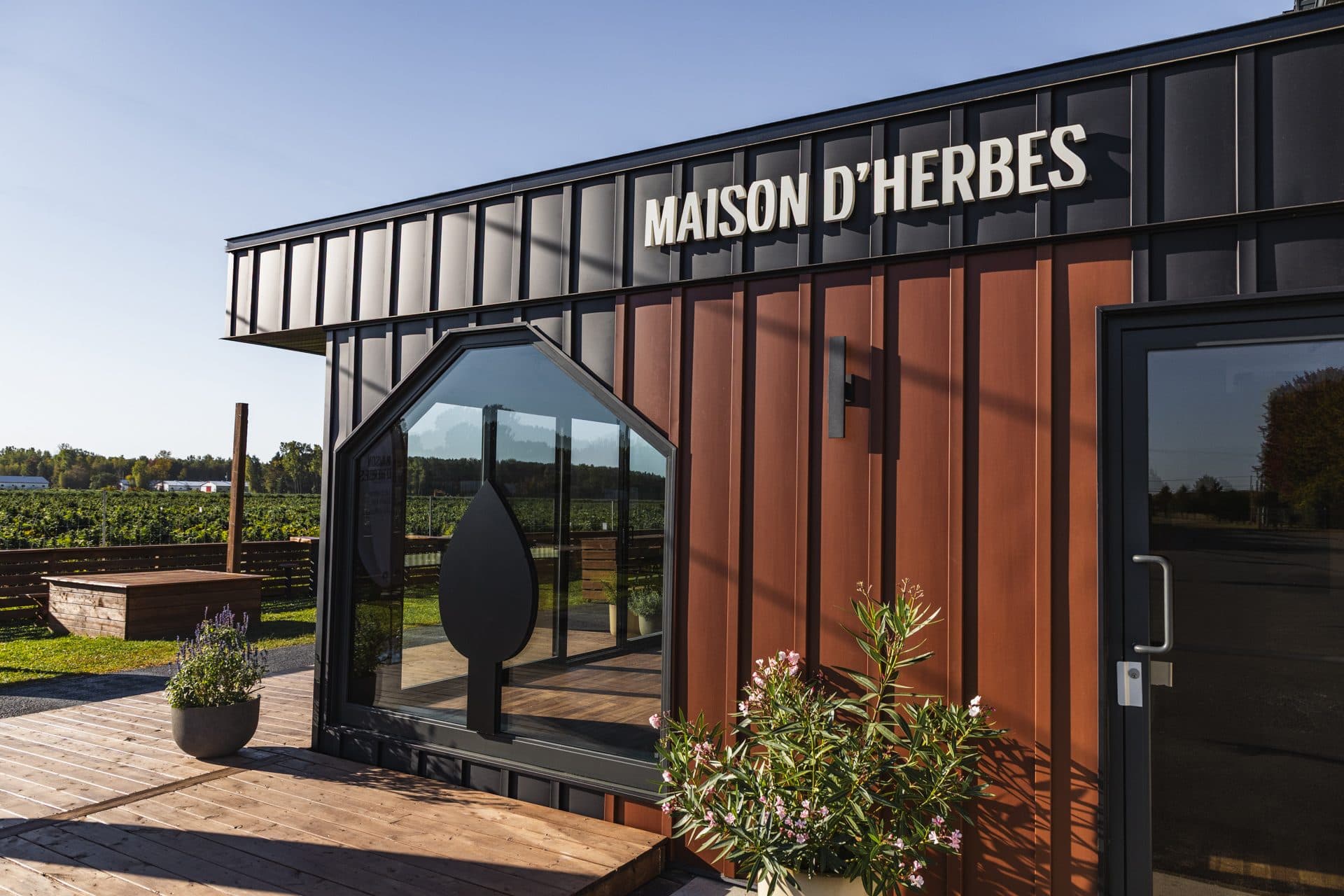 La façade de la boutique Maison d'Herbes à la ferme, son enseigne et sa terrasse de bois, un jour de soleil