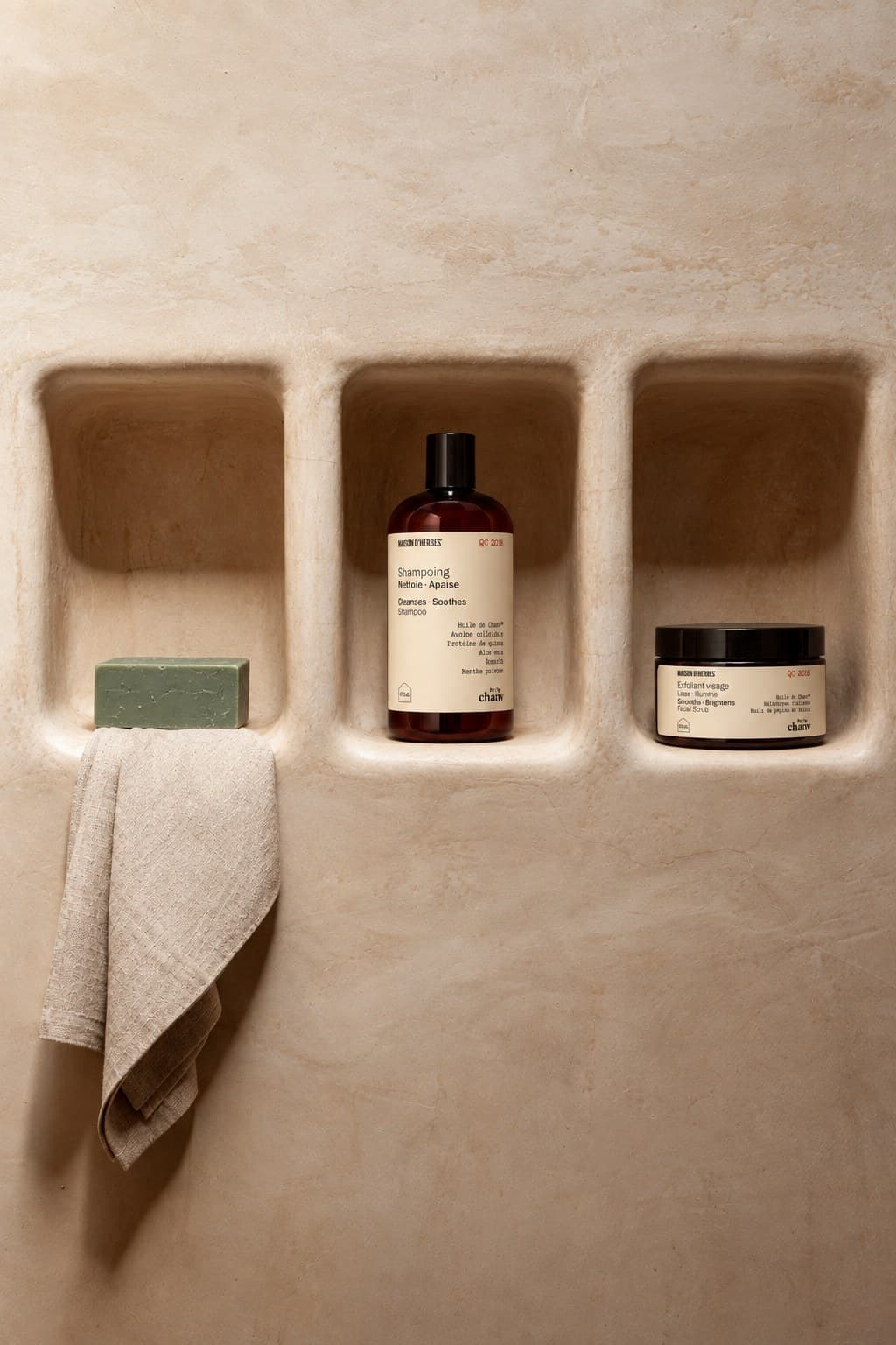 Trois niches de plâtre beige abritant un savon vert, un shampooing et un pot d’exfoliant visage Maison d’Herbes