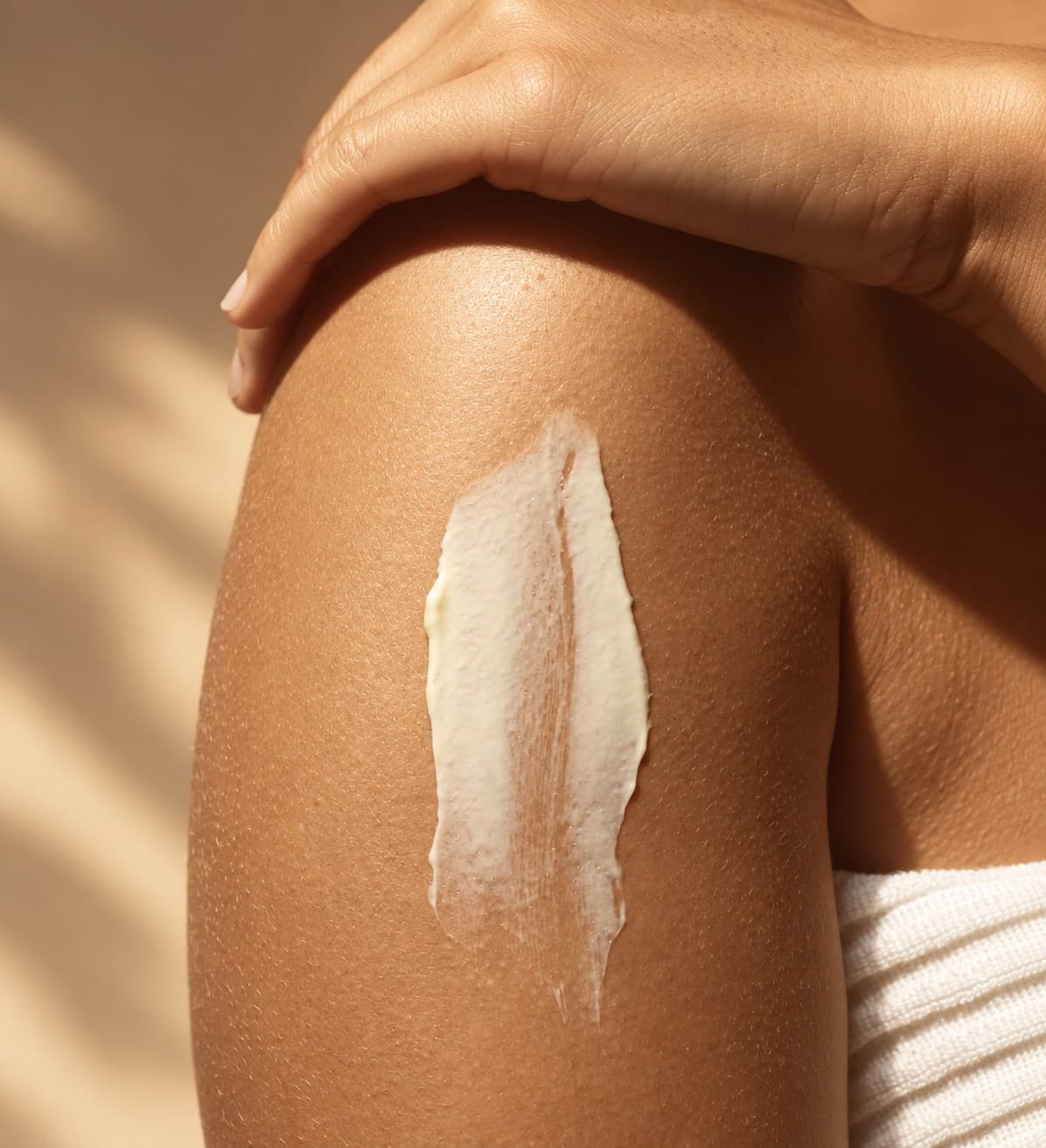 Trait de crème étalé sur un bras nu au soleil, la main remonte vers l’épaule